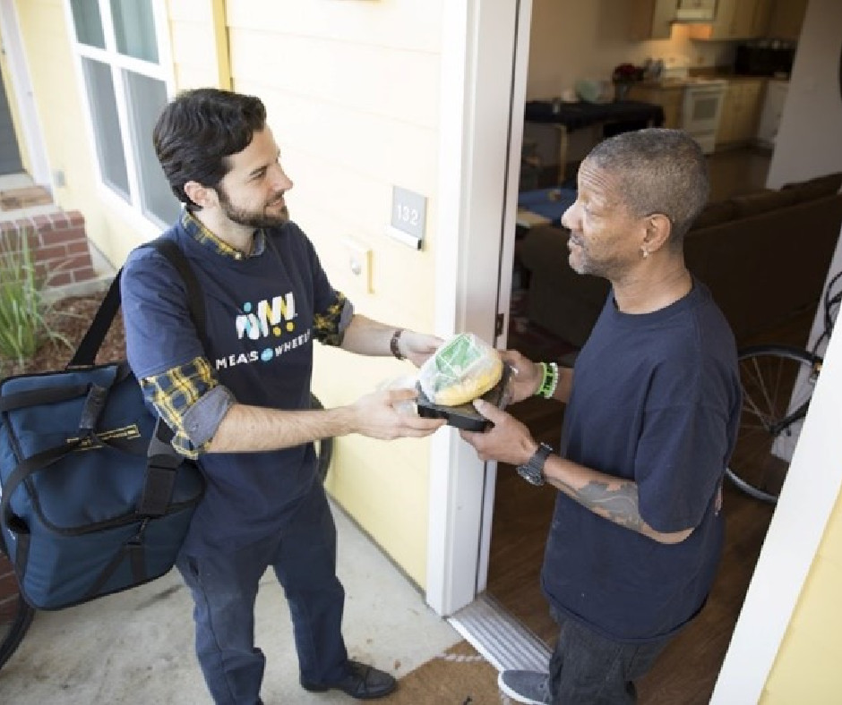A Meals on Wheels volunteer delivering a meal to a grateful neighbor