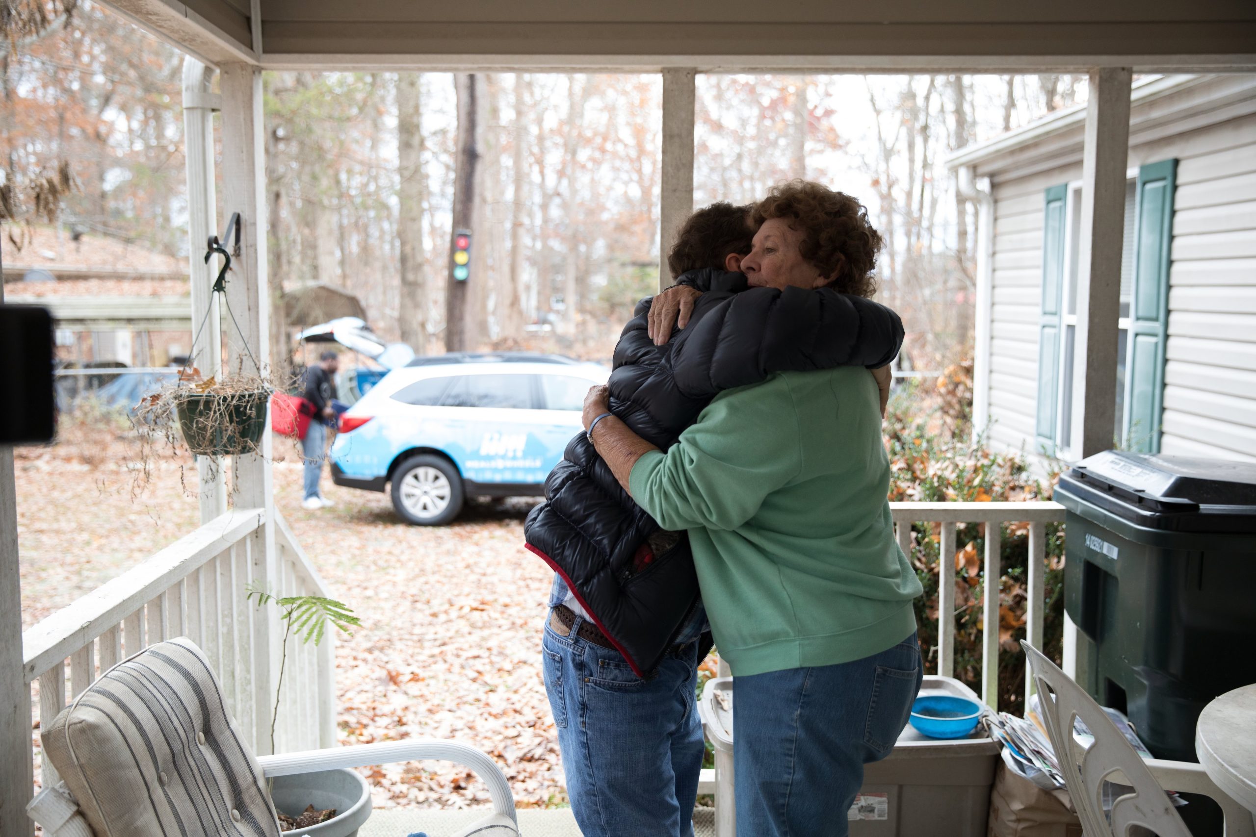 A volunteer and client sharing a warm embrace on a front porch